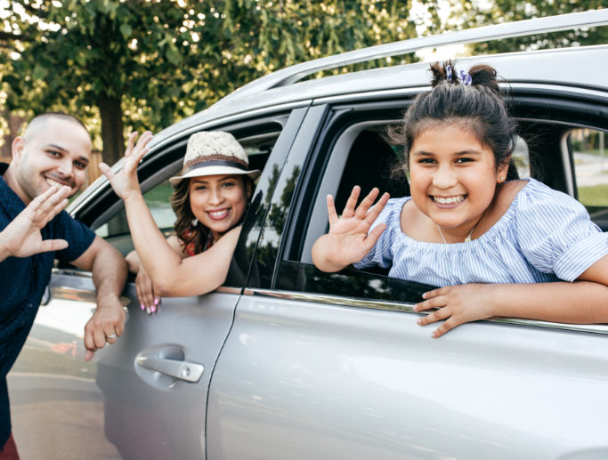 Happy family waving from their car, representing the peace of mind provided by comprehensive auto insurance coverage.