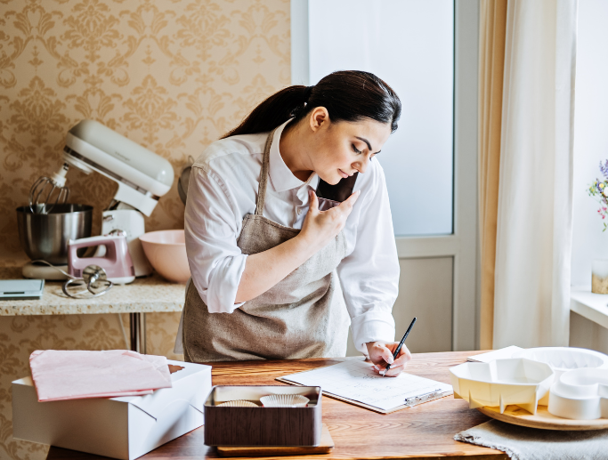 Small business owner working on paperwork in her kitchen, discussing insurance needs over the phone.